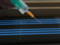 You can see a syringe with liquid, an adhesive agent, which is directed onto small high-purity plastic tubes and apparently connects these tube elements together to create a multiple tube for semiconductor technologies