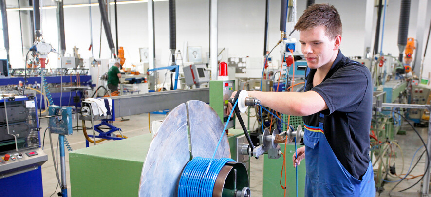 Ein Mitarbeiter der Novoplast produziert an einer Maschine einen blauen Glattschlauch.
