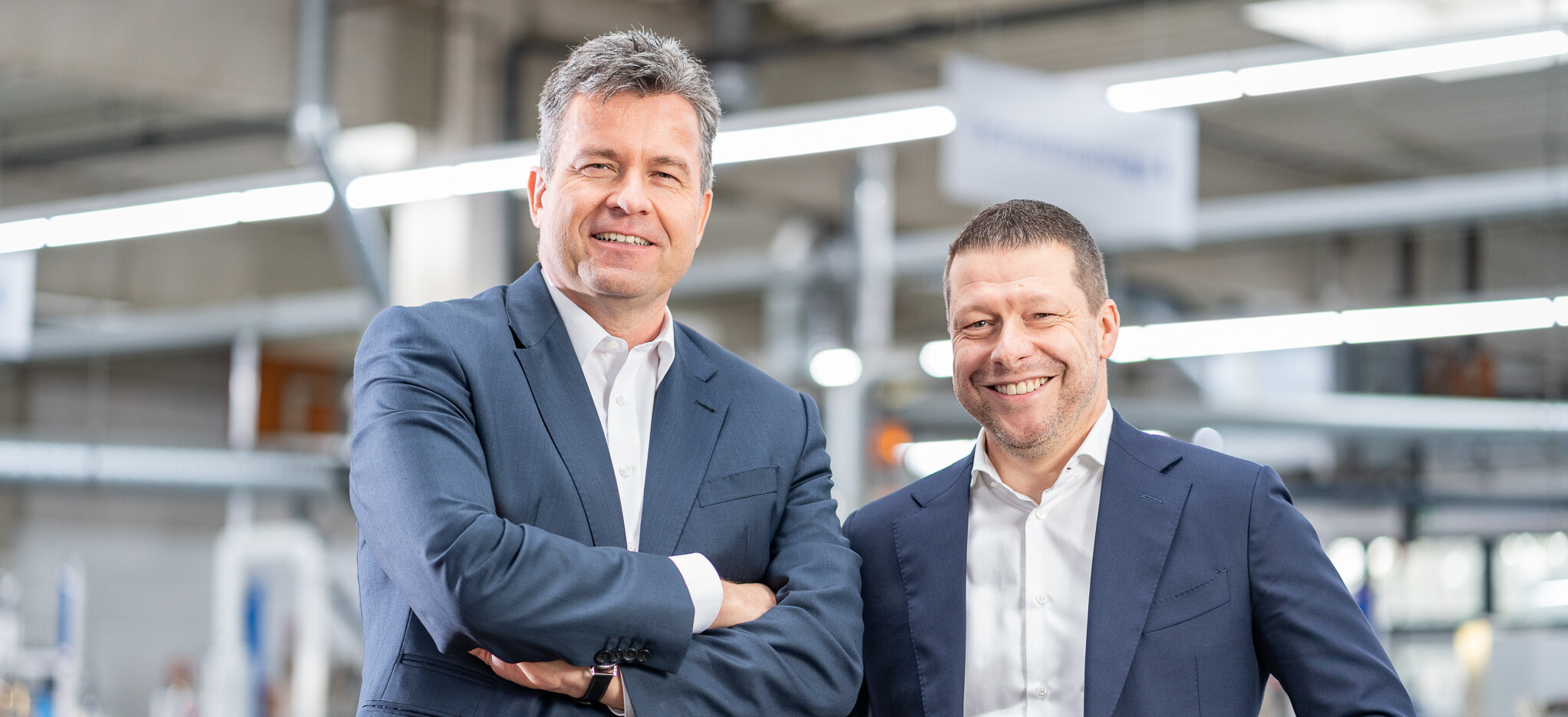 Die Vorstandsmitglieder stehen lächelnd in einer Produktionshalle der Masterflex SE.. 