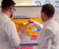 2 Mitarbeiter stehen vor einem Flipchart mit vielen Postit mit Gedanken aus einem Desing Thinking Workshop.